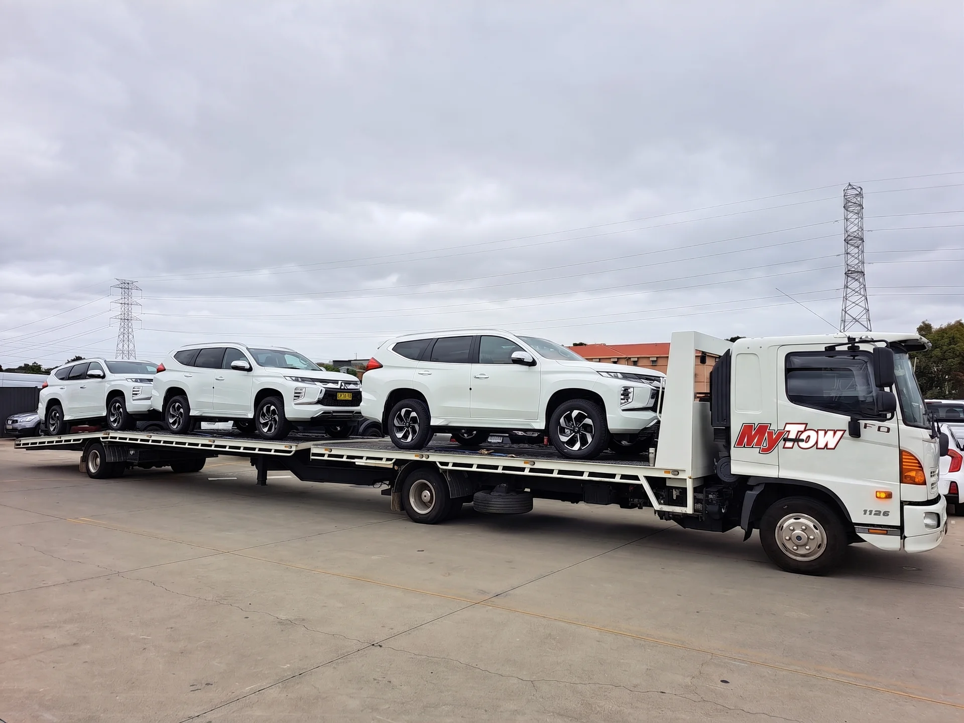 Tow truck carrying three white SUVs